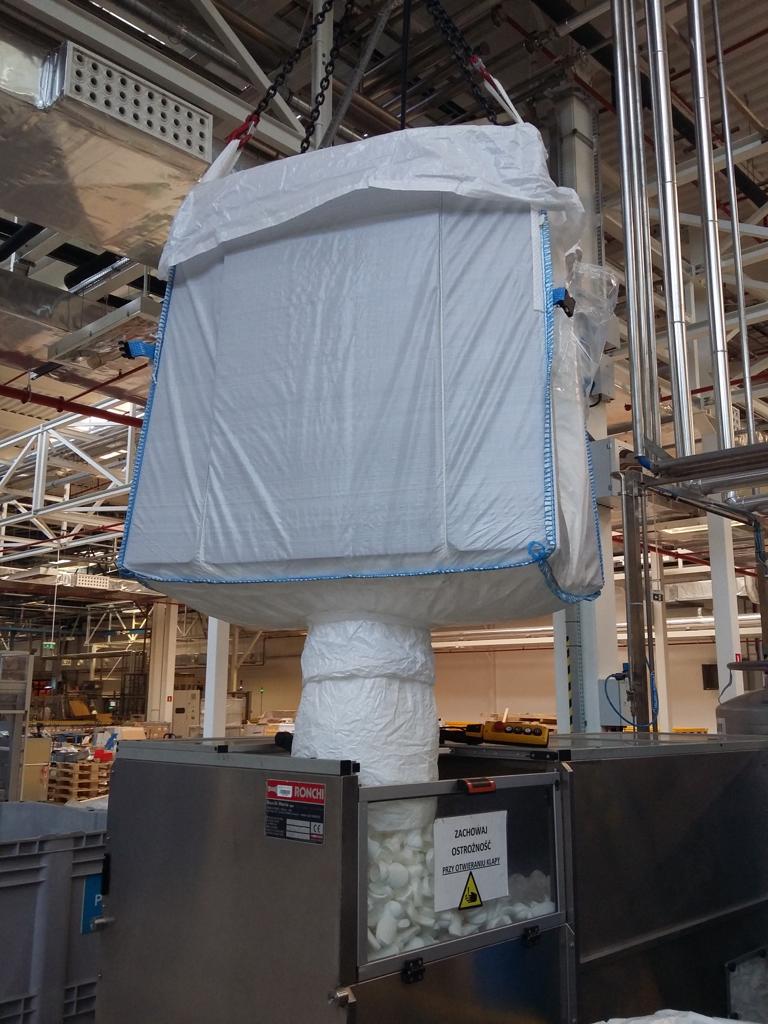 A crane lifting a large white industrial bag labeled with Polish text